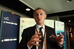 Man in a suit speaking and gesturing with hands at a conference.
