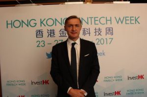 Man in a suit standing at a conference with a tech event backdrop.