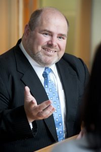 A smiling man in a suit engaging in conversation.