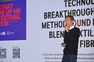 A man presenting in front of a screen with tech-related text.