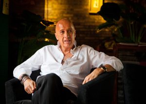 A man in a white shirt sitting comfortably in a dimly lit room.