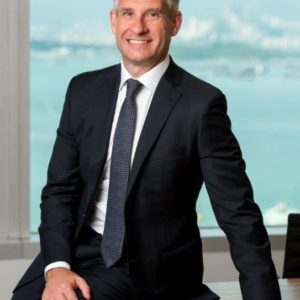 Confident businessman in a suit sitting by a window with a city view.