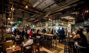 A bustling bar filled with people socializing under warm lighting.