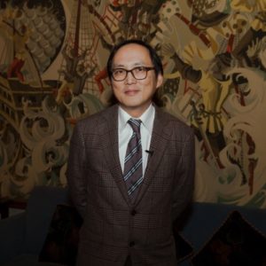 Man in glasses and suit standing in front of a dragon mural.