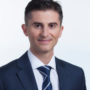Professional man in a suit smiling against a plain background.