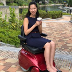 Woman in navy dress sitting on red mobility scooter holding a coffee cup outdoors.