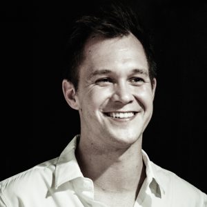Smiling man in a white shirt against a black background.