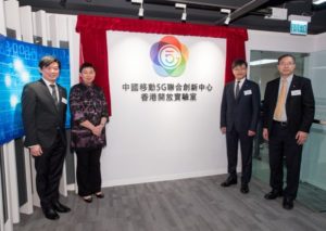 Four individuals standing beside a colorful logo on a white wall.