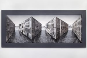 Black and white photo of two buildings reflected on water, creating a mirrored effect.