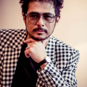 Man wearing sunglasses and checkered blazer posing thoughtfully.