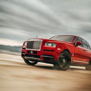 A red luxury SUV speeding on a sandy terrain under a cloudy sky.