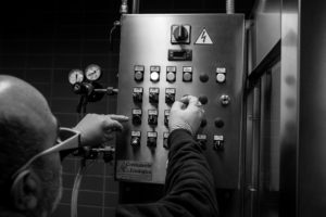 A person operating an industrial control panel with numerous buttons and gauges.