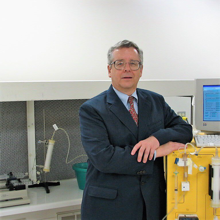 A professional man in a suit stands confidently by scientific equipment.