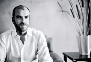 Black and white portrait of a bearded man in a white shirt smiling.