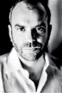 High-contrast black and white portrait of a man with intense eyes and a beard.