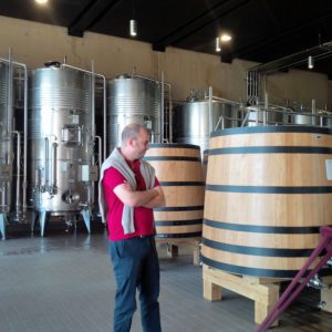 Man standing inside a brewery near large metal and wooden fermentation tanks.