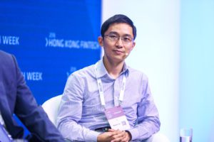 A man wearing glasses and a light purple shirt at a conference.