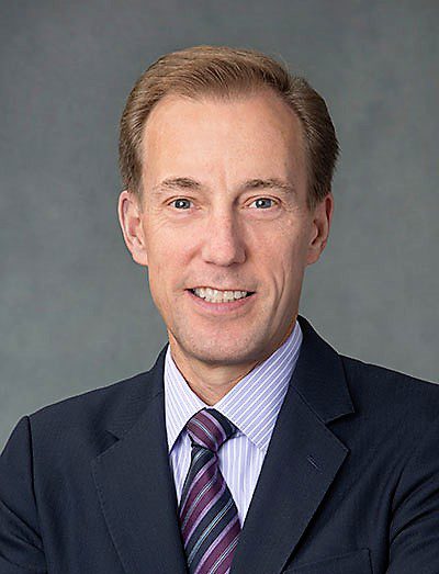 Professional man in suit smiling against gray background.