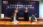 Two individuals sign documents at a formal ceremony with a backdrop of Chinese text.