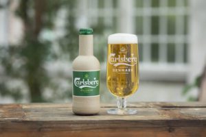 Carlsberg beer bottle and filled glass on wooden table outdoors.