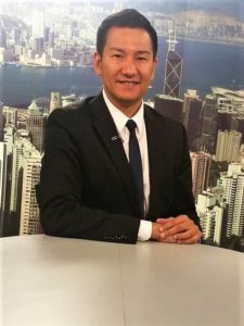 A man in a suit sitting at a desk with a cityscape background.