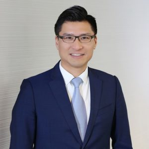 Professional man in a blue suit and glasses smiling.