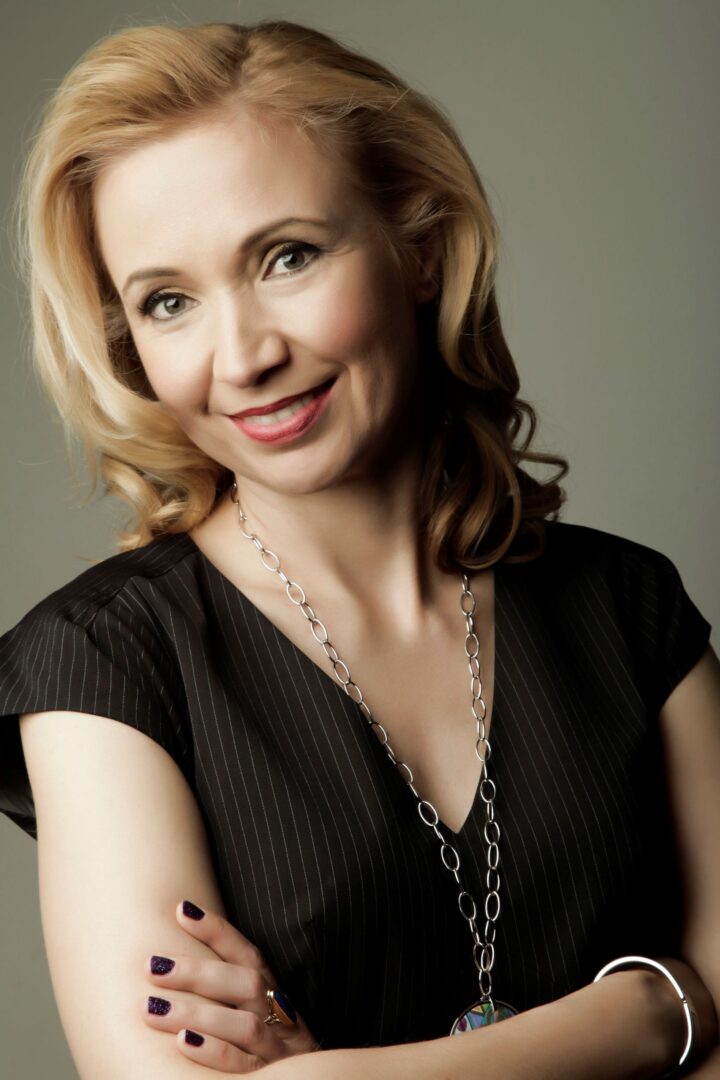 Smiling blonde woman in a black dress with a necklace.