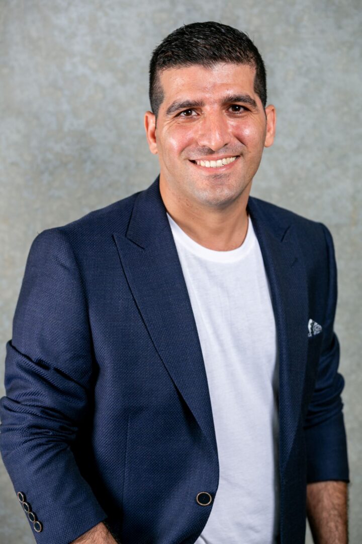Man in a navy blazer and white shirt smiling.