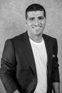 Black and white portrait of a smiling man in a blazer and white shirt.