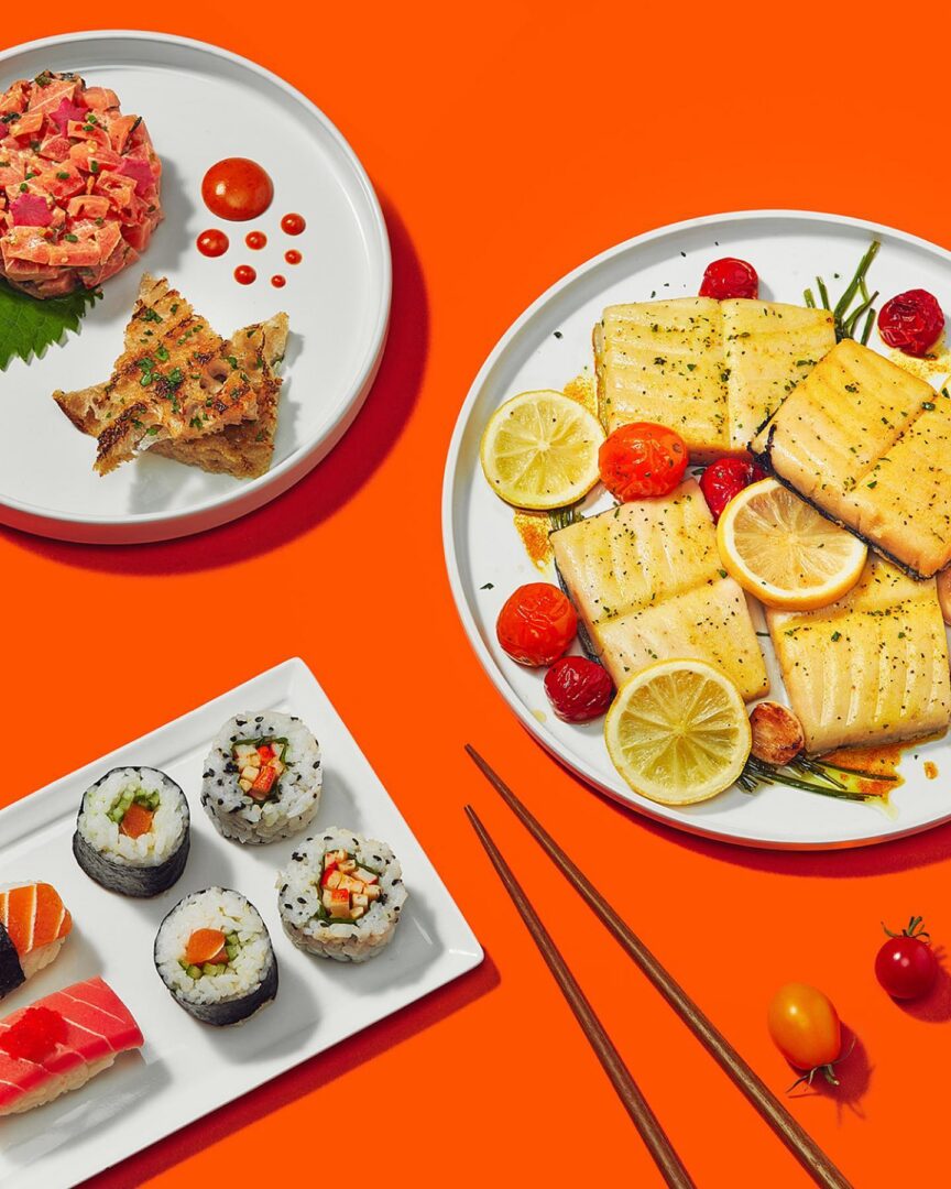 A vibrant spread of sushi, grilled fish, and garnishes on an orange table.