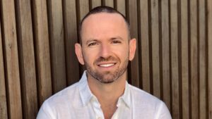 A man smiling in front of a wooden wall.