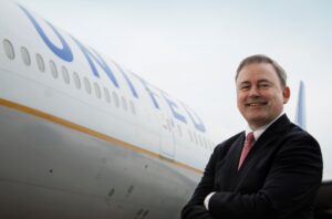 A confident man in a suit standing in front of a United Airlines airplane.