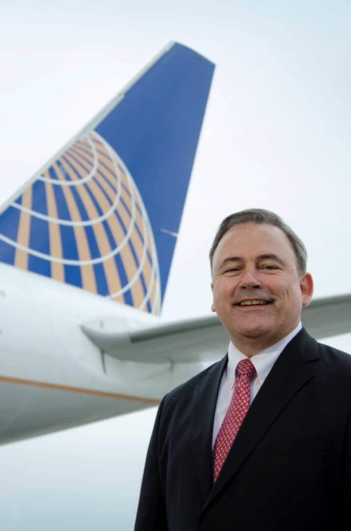 A man in a suit standing near a United Airlines plane.