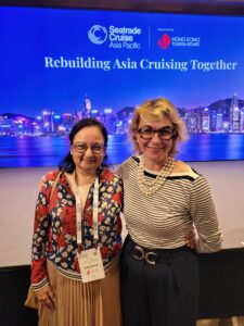 Two women smiling at an Asia Cruise event with a city skyline backdrop.