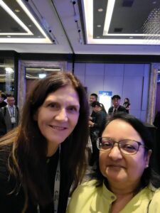 Two women smiling at a conference or event indoors.