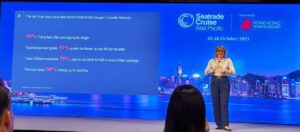 Speaker presenting Seatrade Cruise Global 2023 event on stage with city skyline background.