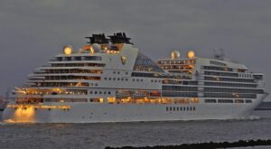 A large cruise ship illuminated at dusk near the shore.