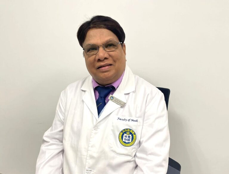 A man in a white medical coat sitting and smiling.