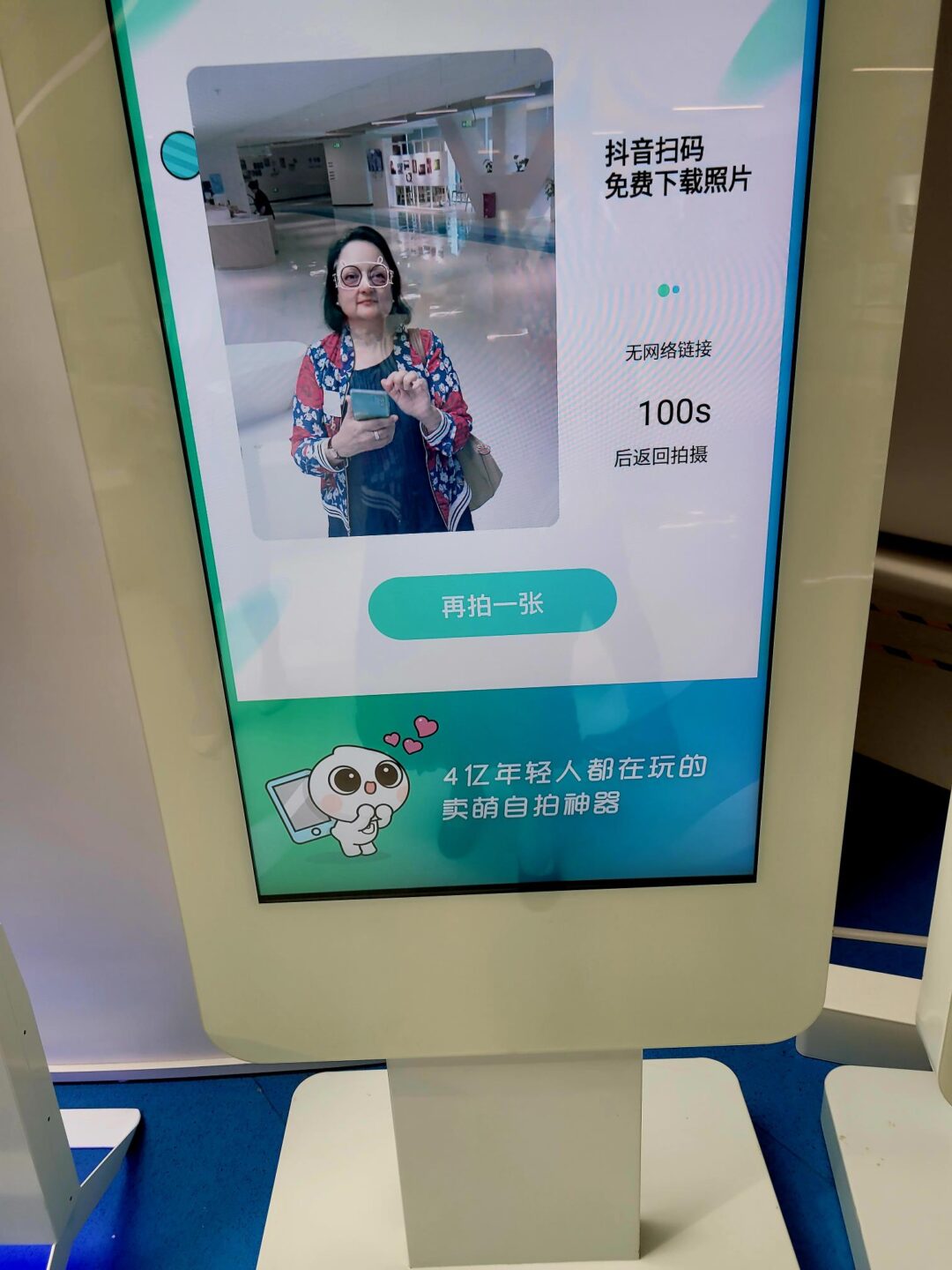 A woman posing for a photo on a digital kiosk screen with Chinese text.