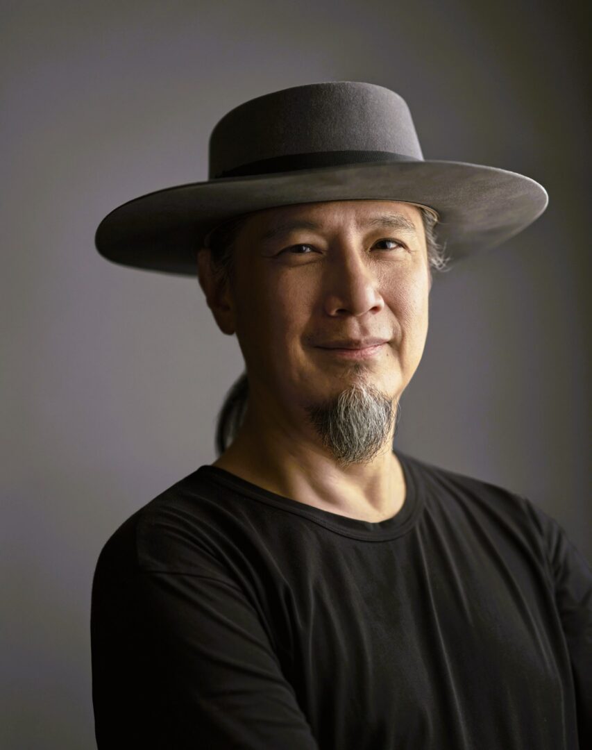 Man with a gray hat and black shirt smiling confidently.